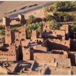 Scenic view of Kasbah Ait Ben Haddou, a UNESCO World Heritage site, surrounded by the arid Moroccan landscape under a clear blue sky.