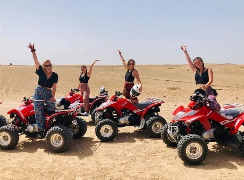 A group of people riding quad bikes in the Agafay Desert, with sand dunes and rocky terrain in the background